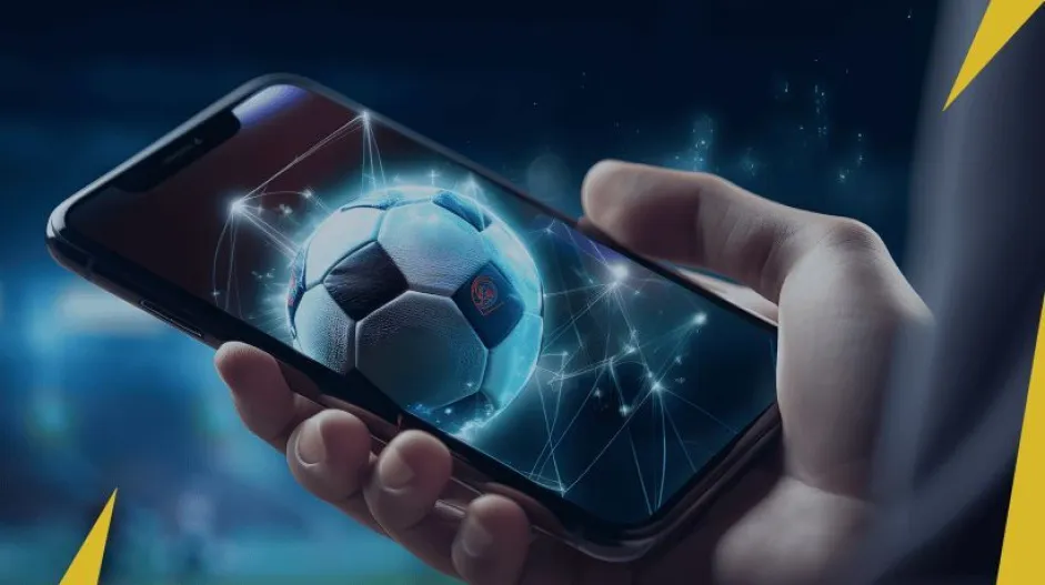 Uma mão segurando um celular com uma bola de futebol na tela, com um texto em amarelo e branco
