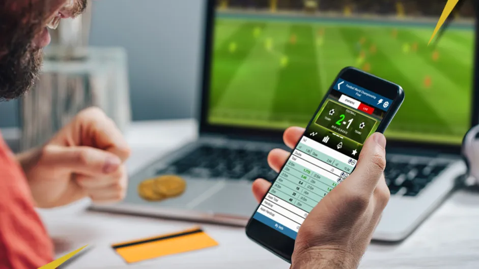 Jogos de apostas de 1 real: na imagem há um homem vendo uma aposta em seu smartphone, a imagem é bem colorida.