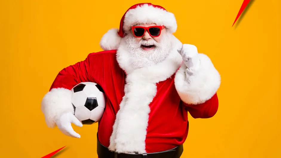 Bonus de Natal: papai noel com uma bola de futebol embaixo do braço, óculos escuros e sinalizando estar tudo bem com a mão esquerda, enquanto sorri, em fundo amarelo